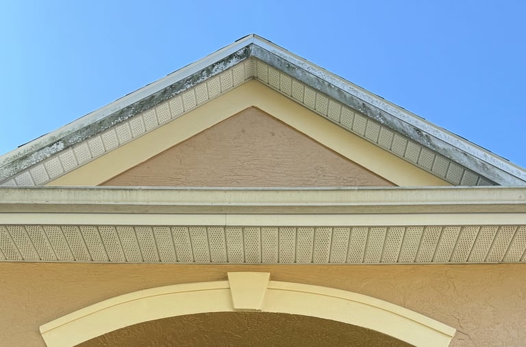 Close-up of a buildings triangular roofline and arched architectural detail against a clear blue sky