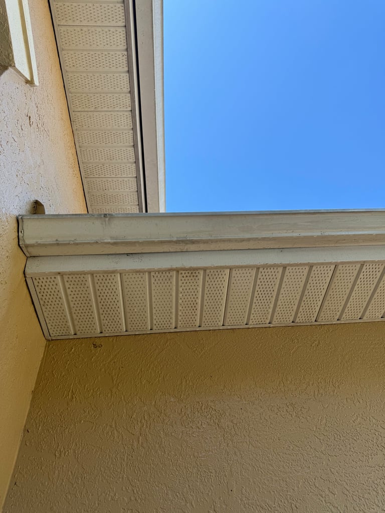 Beige soffit with perforated vents under building eave against clear blue sky