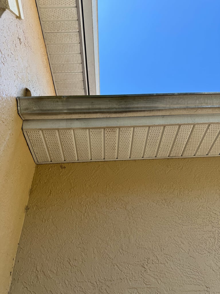 Close-up of exterior building soffit and trim with metal edging against textured beige wall and clear blue sky